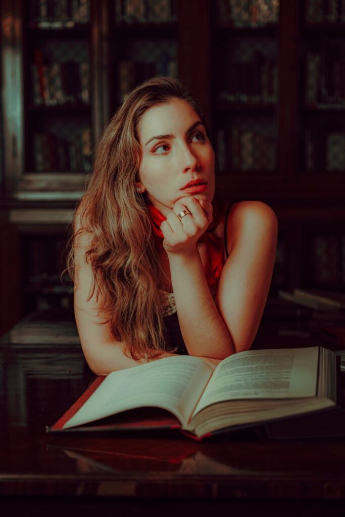 A contemplative woman sits in a library with an open book, deep in thought.